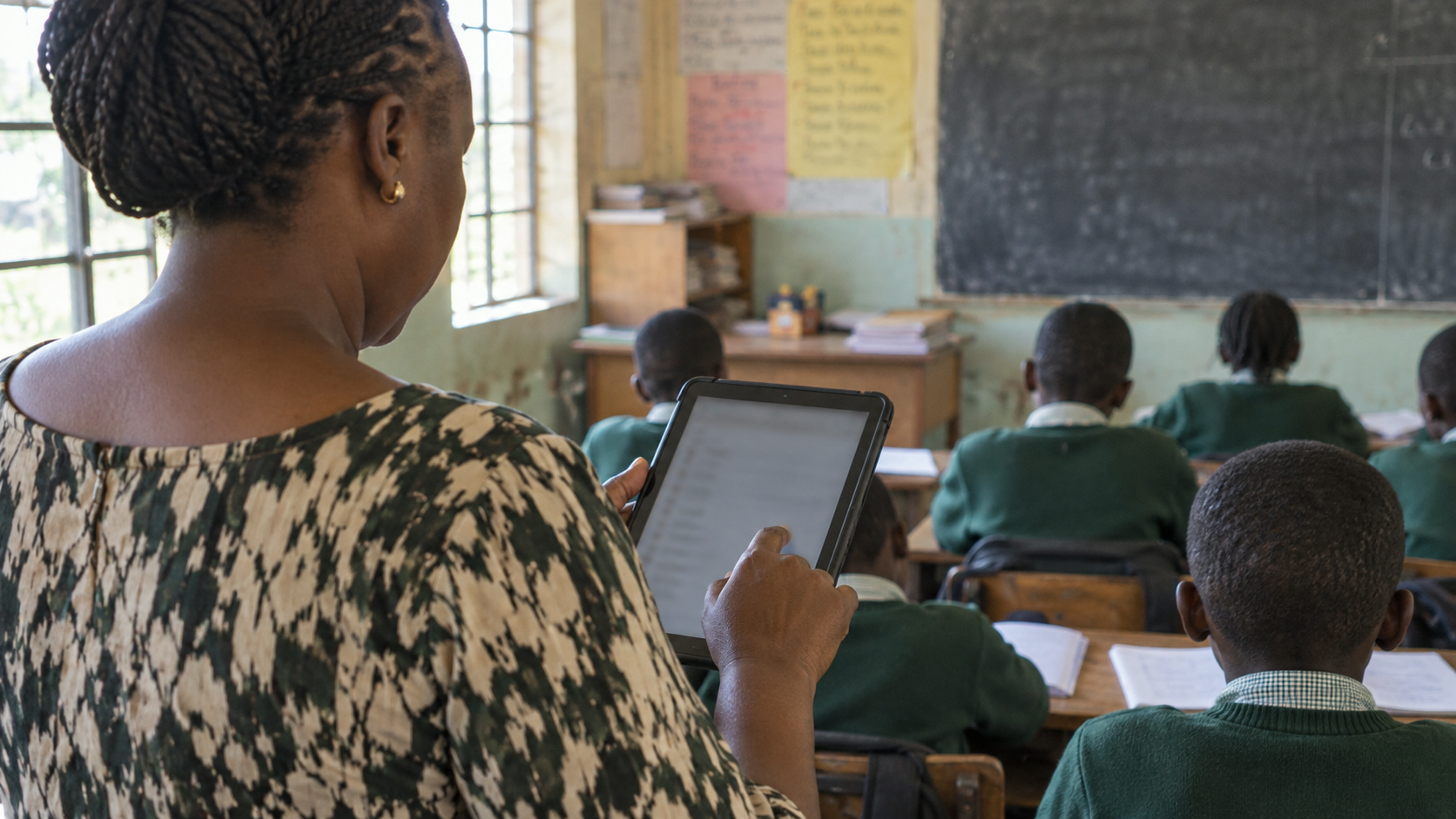 Over-shoulder of a teacher ticking attendance on a tablet.