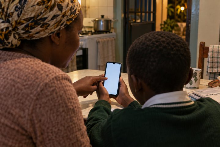 A child and parent sit at a kitchen table with a phone showing a daily challenge.