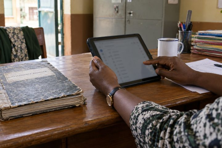 A closed paper attendance register pushed aside beside a tablet.