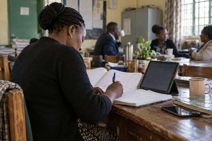 A teacher writes into a CBC scheme of work at a staffroom table.