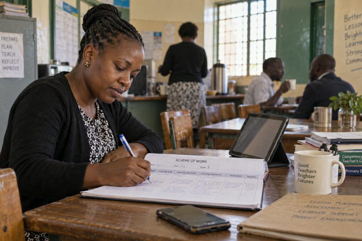 A teacher writes into a scheme of work at a staffroom table before school.
